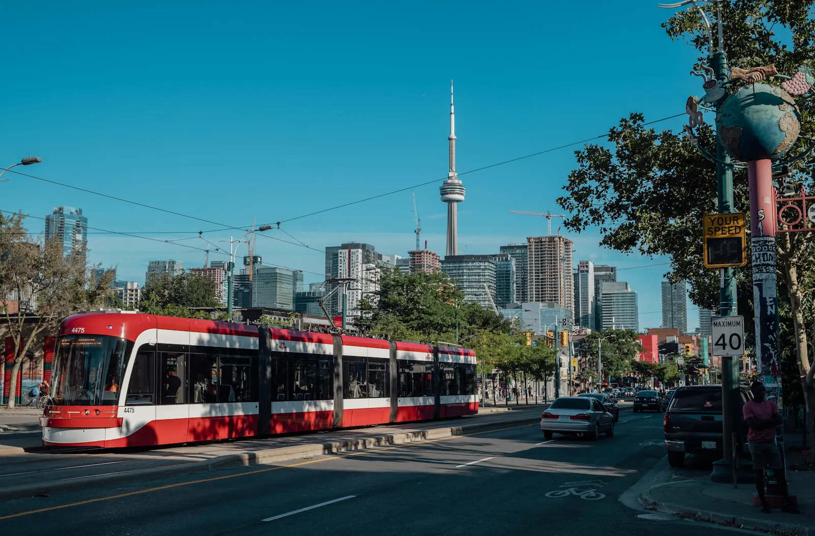 A red Toronto streetcar passing through the city, with the CN Tower behind it
